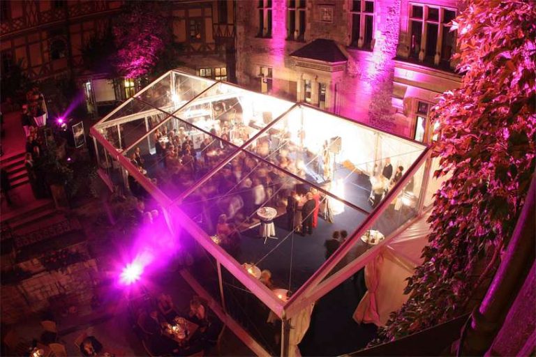 Partyzelt mit transparentem Dach zur Miete während einer Abendveranstaltung mit bunter Beleuchtung und vielen Gästen